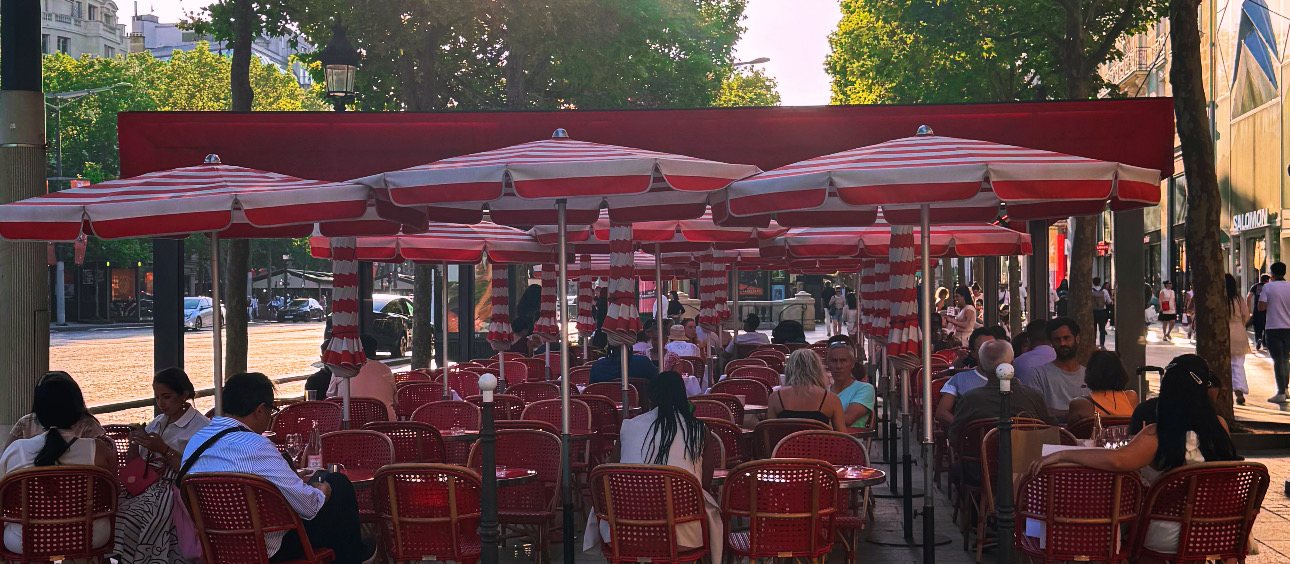 A Parisian café terrace under red umbrellas at dusk